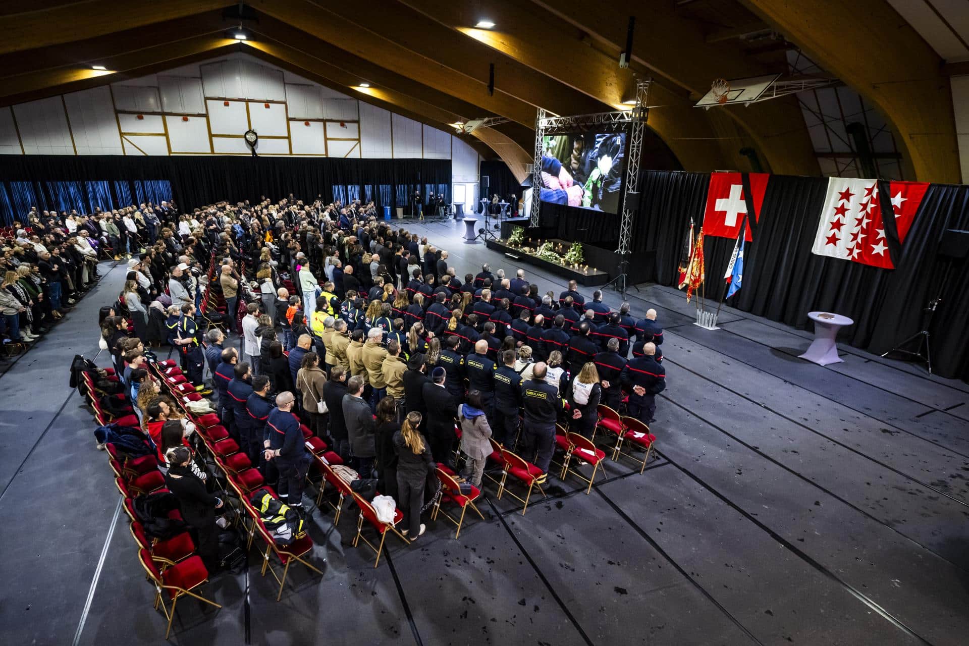 La gente observa un minuto de silencio en memoria de las víctimas mientras ven en una pantalla en el 'Le Regent Congress hall' la ceremonia conmemorativa oficial durante el día nacional de luto tras el incendio mortal en el bar 'Le Constellation' en Crans-Montana, en el Centro de Exposiciones y Convenciones (CERM) de Martigny, Suiza, 09 de enero de 2026. 40 personas, en su mayoría adolescentes, perdieron la vida y 116 resultaron gravemente heridas en el incendio en el bar 'Le Constellation' durante la celebración de Año Nuevo en el balneario alpino suizo de Crans-Montana. (Suiza) EFE/EPA/JEAN-CHRISTOPHE BOTT