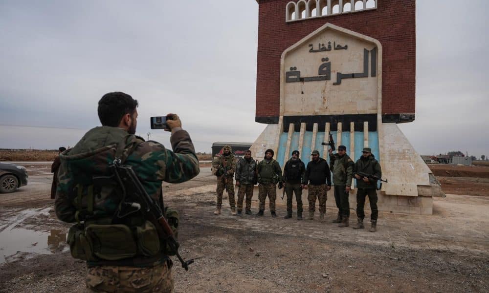 Miembros del ejército sirio se encuentran frente a un letrero que dice "Raqqa te da la bienvenida" después de la retirada de las Fuerzas Democráticas Sirias lideradas por los kurdos en la aldea de Al-Ghamiz, en el campo de Raqqa, Siria, 17 de enero de 2026. (Siria) EFE/EPA/AHMAD FALLAHA