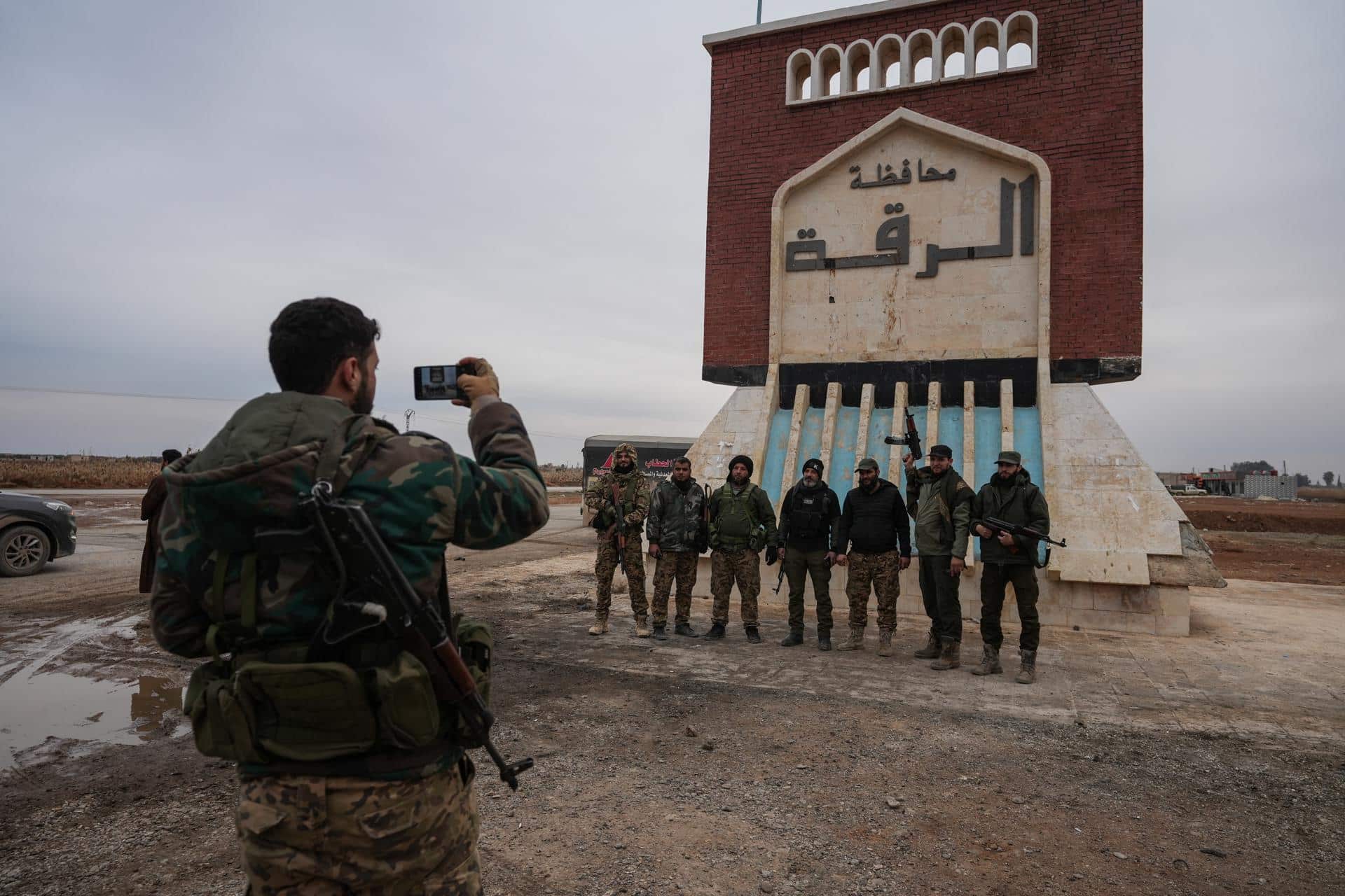 Miembros del ejército sirio se encuentran frente a un letrero que dice "Raqqa te da la bienvenida" después de la retirada de las Fuerzas Democráticas Sirias lideradas por los kurdos en la aldea de Al-Ghamiz, en el campo de Raqqa, Siria, 17 de enero de 2026. (Siria) EFE/EPA/AHMAD FALLAHA