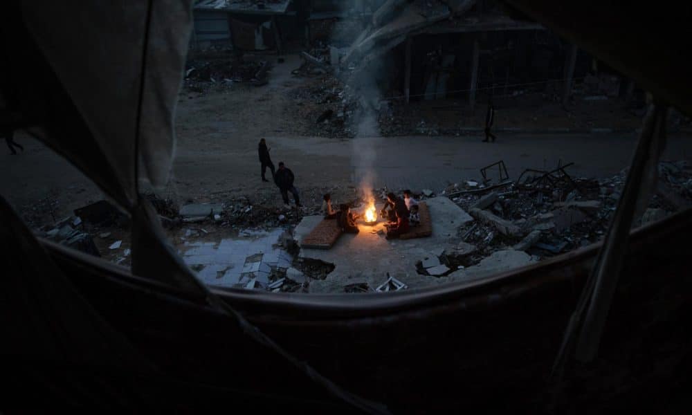 Palestinos desplazados se calientan cerca de un fuego entre las ruinas de su hogar destruido en Khan Yunis, en la franja de Gaza sur, el 30 de diciembre de 2025, en medio de un alto el fuego entre Israel y Hamas. 
EFE/EPA/HAITHAM IMAD
