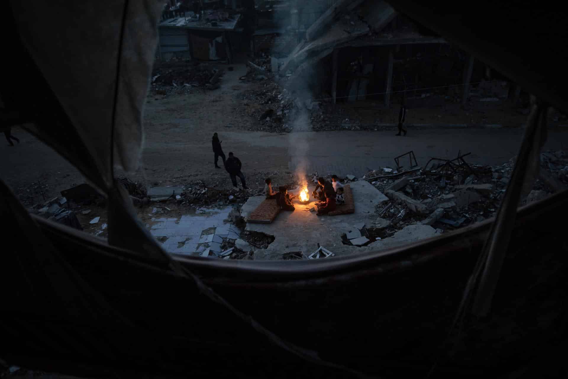 Palestinos desplazados se calientan cerca de un fuego entre las ruinas de su hogar destruido en Khan Yunis, en la franja de Gaza sur, el 30 de diciembre de 2025, en medio de un alto el fuego entre Israel y Hamas. 
EFE/EPA/HAITHAM IMAD