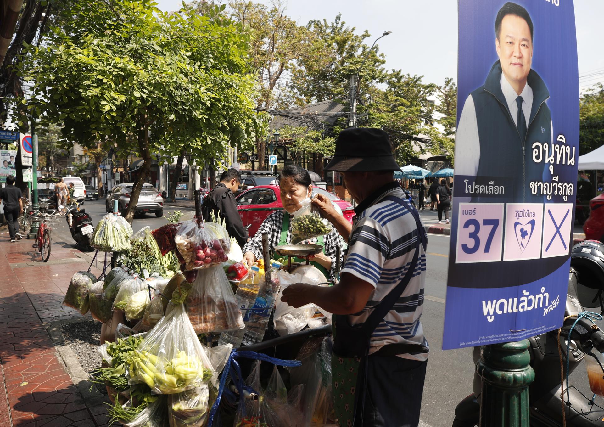Bangkok (Tailandia), 04/02/2026.- Un vendedor ambulante vende verduras junto a un cartel de la campaña electoral del primer ministro tailandés y líder del partido conservador Bhumjaithai, Anutin Charnvirakul, en Bangkok. EFE/EPA/RUNGROJ YONGRIT