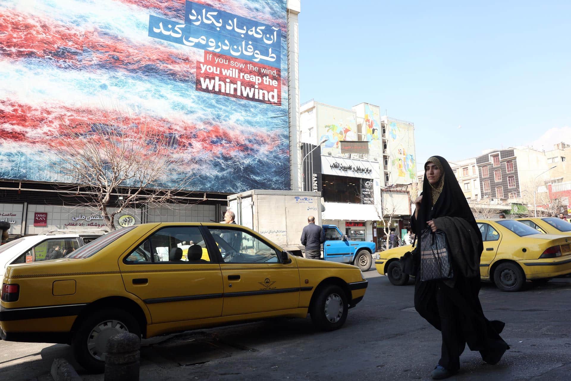 Una mujer iraní pasa frente a un cartel antiestadounidense en Teherán, Irán, el 25 de febrero de 2026. Irán y Estados Unidos mantienen este jueves una tercera ronda de negociaciones en Ginebra en busca de un acuerdo nuclear en medio de las amenazas de una intervención armada del presidente estadounidense, Donald Trump, quien ha realizado el mayor despliegue militar en Oriente Medio desde la guerra de Irak.  EFE/EPA/ABEDIN TAHERKENAREH