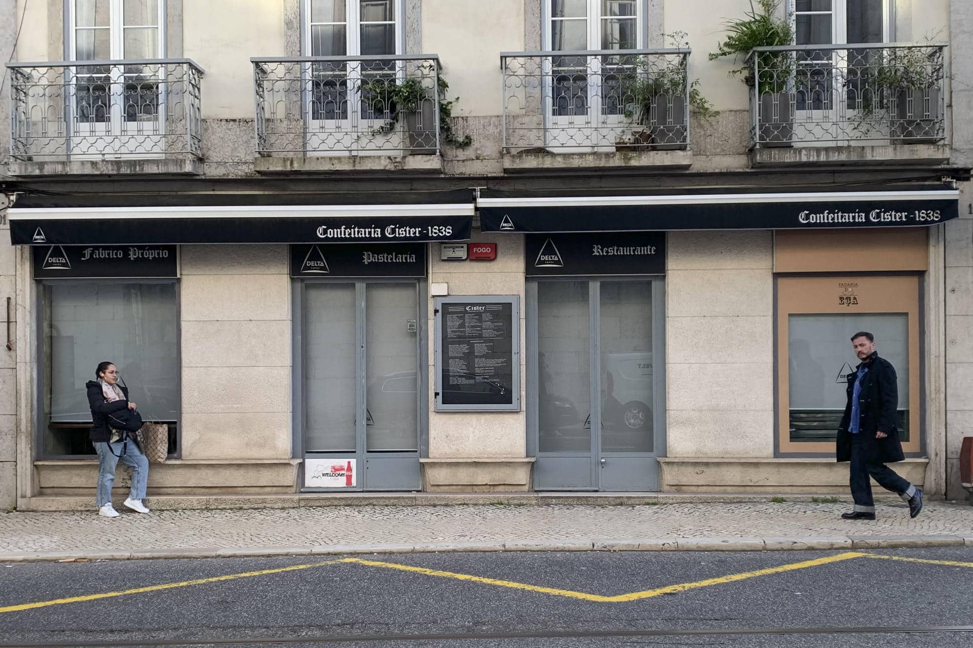 Vecinos pasan por delante de la Confeitaría Cistér, cafetería cerrada en diciembre de 2025. Lisboa se está quedando huérfana de las cafeterías y pastelerías tradicionales que han acompañado a muchas generaciones, ante una oleada de cierres derivada del alto precio de los alquileres y el turismo masivo, para el que se abren otro tipo de establecimientos. Muchas de ellas, con décadas e incluso algún siglo de historia, dan paso a comercios orientados a los visitantes como hostales, consignas o franquicias internacionales, dejando atrás la idiosincrasia de los barrios y poniendo en contra a sus residentes.- EFE/ Blas Díaz