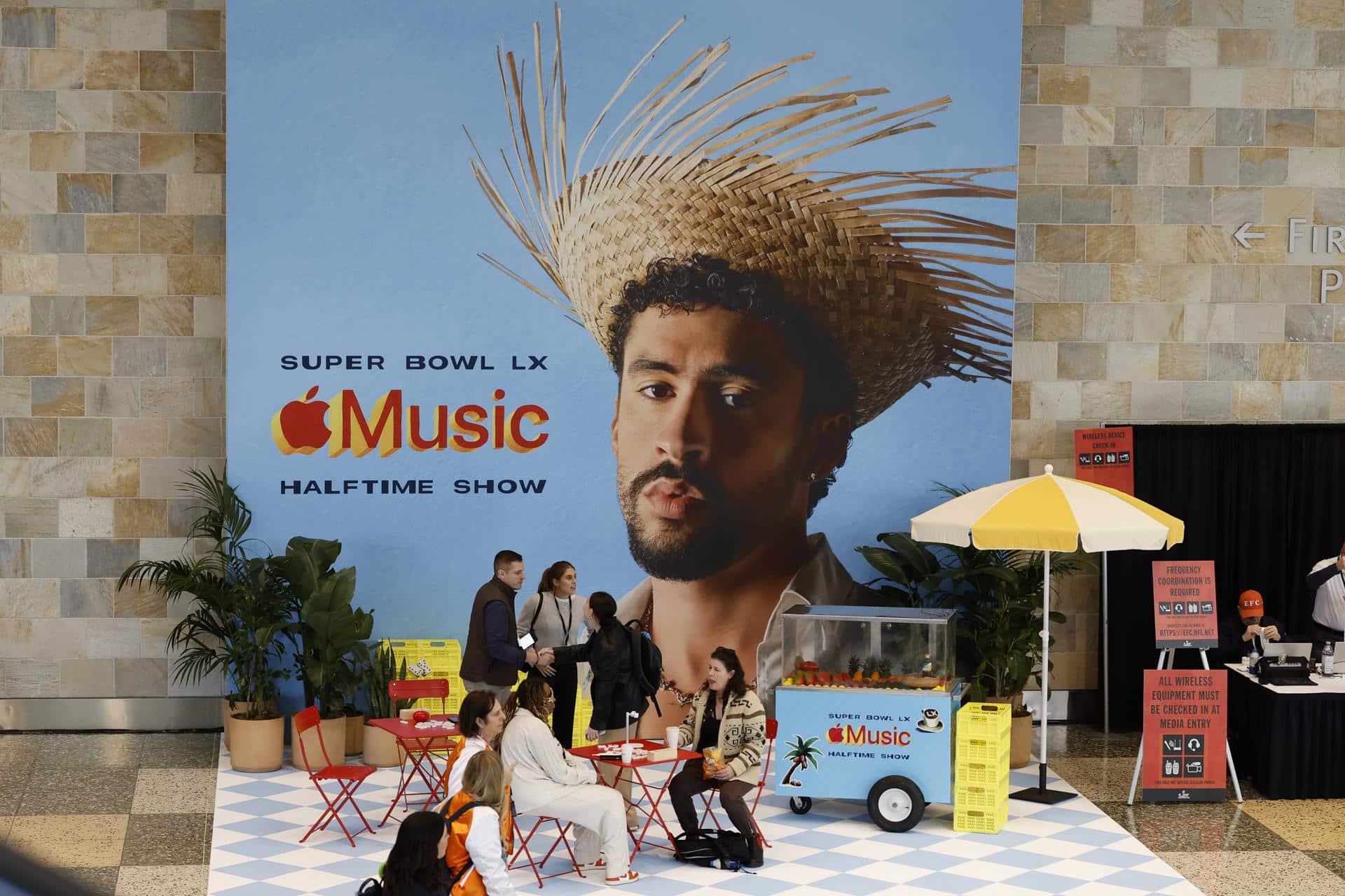 Gente sentada junto a un cartel del cantante Bad Bunny, protagonista del espectáculo del medio tiempo del Super Bowl, que se disputa este domingo. EFE/EPA/JOHN G. MABANGLO
