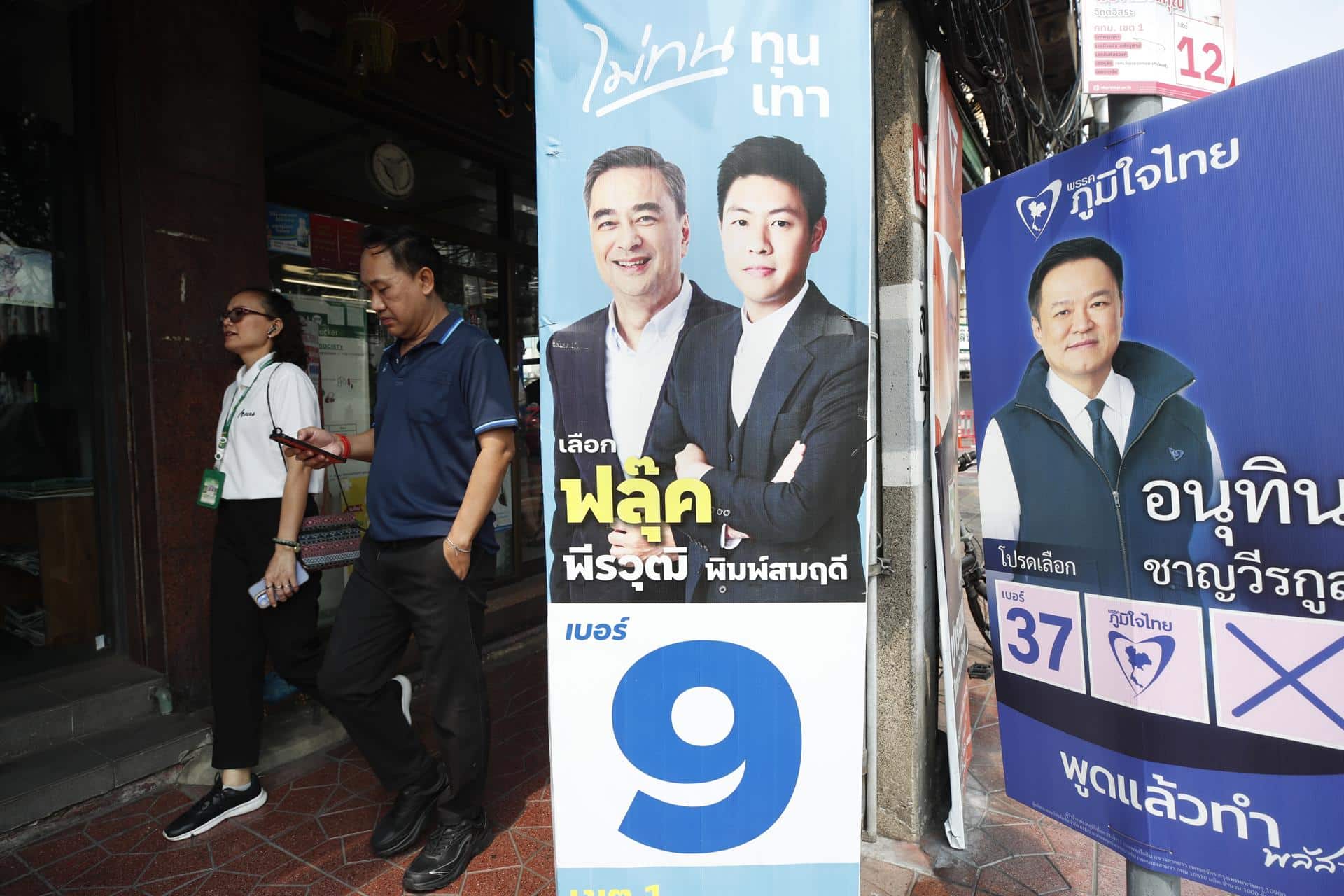 Bangkok (Tailandia), 04/02/2026.- Personas caminan junto a carteles de la campaña electoral del líder del Partido Demócrata y ex primer ministro Abhisit Vejjajiva (izq.) y del primer ministro tailandés y líder del Partido Bhumjaithai, Anutin Charnvirakul (der.), en Bangkok, Tailandia, el 4 de febrero de 2026. EFE/EPA/RUNGROJ YONGRIT