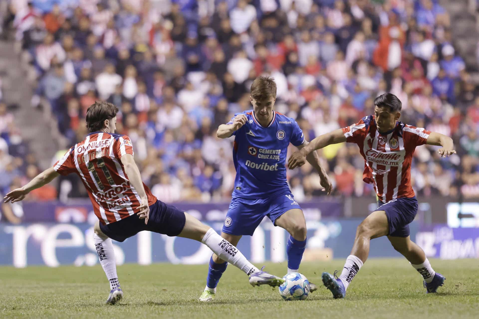 Agustín Palavecino (c), de Cruz Azul, disputa el balón con Brian Gutierrez (i) y Ángel Sepúlveda (d), de Guadalajara durante un partido de la jornada 7 del torneo Apertura 2026 de la Liga MX entre Cruz Azul y Guadalajara en el estadio Cuauhtémoc en Puebla (México). EFE/Hilda Ríos