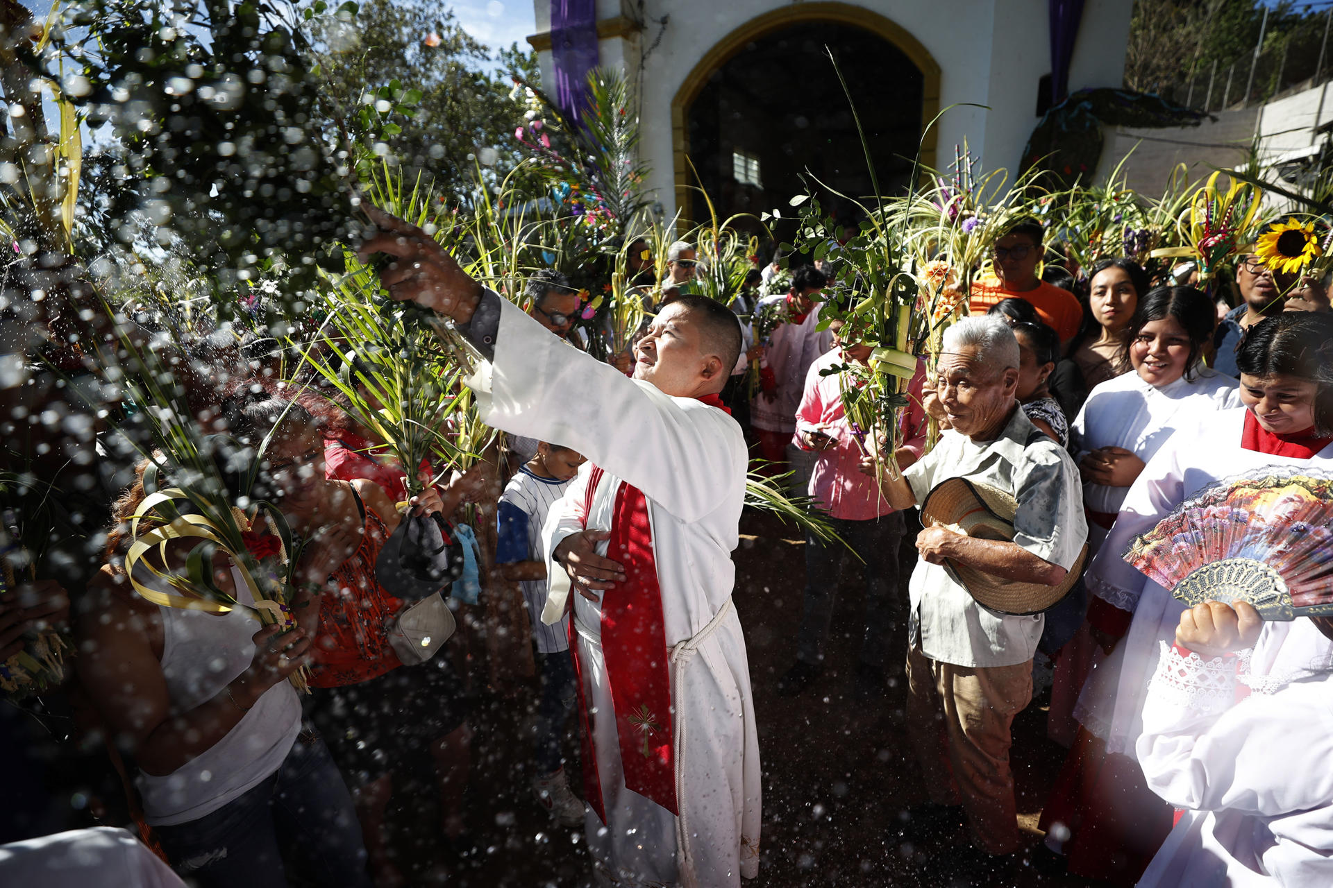 Un sacerdote esparce agua bendita durante la procesión del Domingo de Ramos en Nahuizalco (El Salvador). EFE/Rodrigo Sura