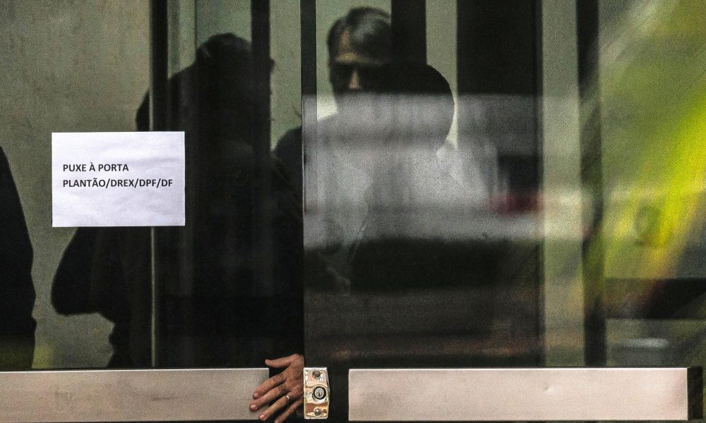 Fotografía de archivo que muestra al expresidente de Brasil Jair Bolsonaro (c) detrás de una puerta de vidrio, en la Superintendencia de la Policía Federal en Brasilia (Brasil). EFE/ Isaac Fontana
