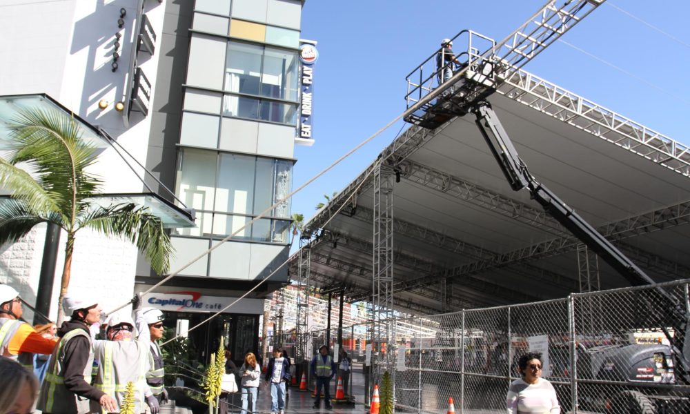 Unas personas caminan frente a una grúa y unos obreros mientras levantan una carpa el pasado jueves 5 de marzo en el bulevar Hollywood, alrededor del Teatro Dolby en Los Ángeles, California. La sesión de embellecimiento del bulevar de Hollywood para recibir a las luminarias en la 98 edición de los Óscar ha comenzado en Los Ángeles con la construcción de un escenario que requiere decenas de obreros, grandes grúas y largas cortinas, que hacen parte de una producción que el año pasado costó cerca de 60 millones de dólares. EFE/Ana Milena Varón