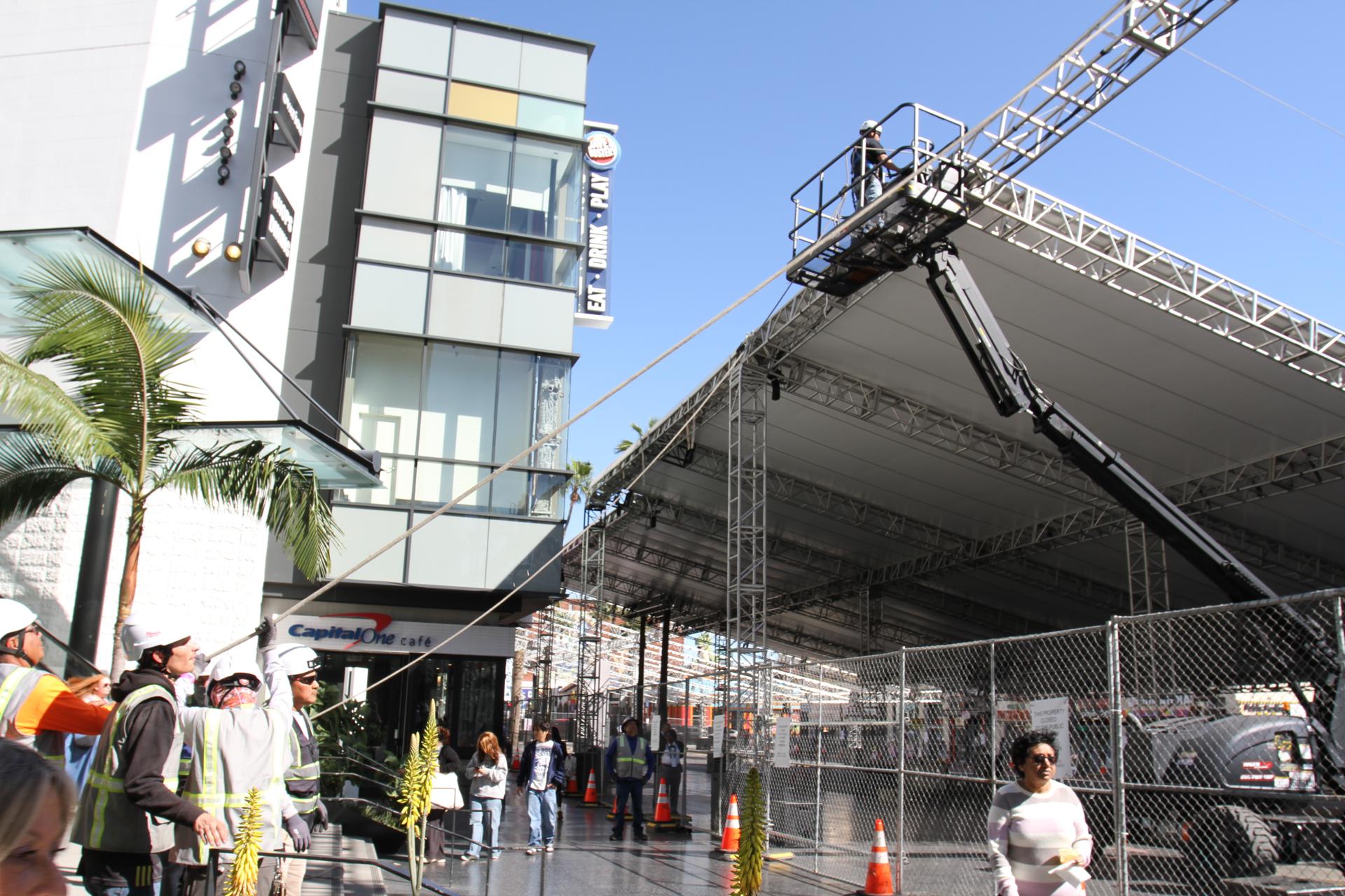 Unas personas caminan frente a una grúa y unos obreros mientras levantan una carpa el pasado jueves 5 de marzo en el bulevar Hollywood, alrededor del Teatro Dolby en Los Ángeles, California. La sesión de embellecimiento del bulevar de Hollywood para recibir a las luminarias en la 98 edición de los Óscar ha comenzado en Los Ángeles con la construcción de un escenario que requiere decenas de obreros, grandes grúas y largas cortinas, que hacen parte de una producción que el año pasado costó cerca de 60 millones de dólares. EFE/Ana Milena Varón