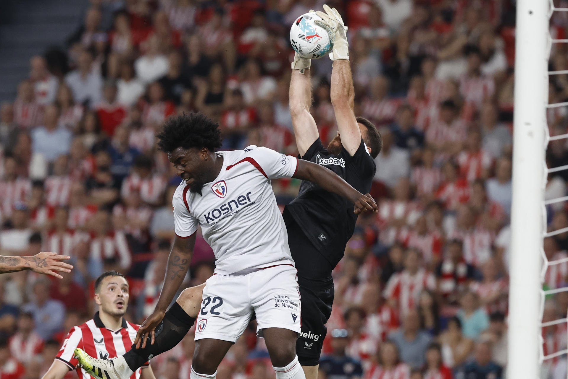 El guardameta del Athletic Unai Simón (d) salta por el balón con Flavien-Enzo Boyomo, de Osasuna, durante el encuentro correspondiente a la jornada 32 de LaLiga que disputaron Athletic Club y Osasuna este martes en el estadio de San Mamés, en Bilbao. EFE / Miguel Toña.