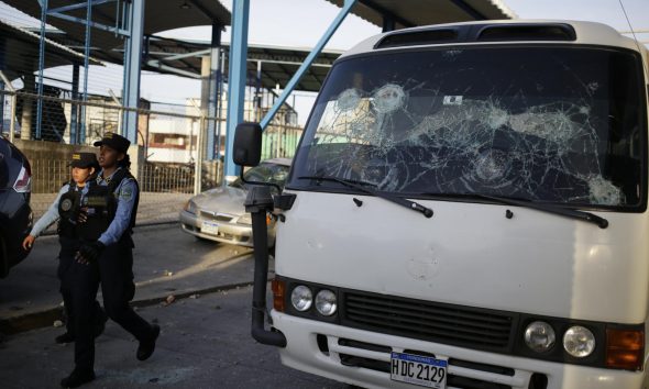 Policías pasan al lado de un vehículo que sufripó daños tras un enfrentamiento entre fanáticos de los equipos Motagua y Olimpia en Tegucigalpa (Honduras). EFE/Gustavo Amador