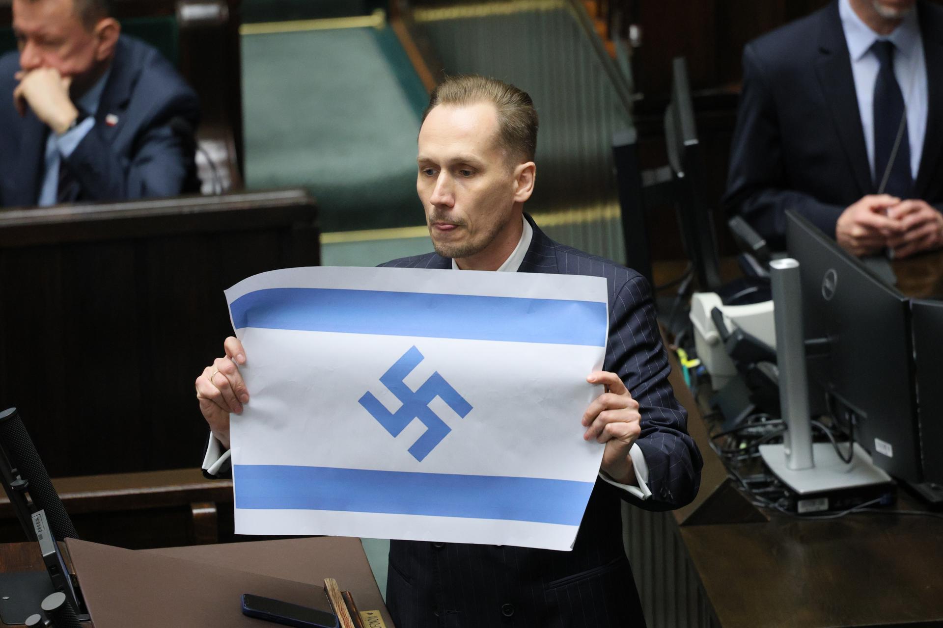 El diputado del partido polaco de extrema derecha Confederación, Konrad Berkowicz, muestra una bandera israelí marcada con una esvástica en el Parlamento polaco en Varsovia, Polonia, el pasado 14 de abril de 2026, cuando acusó a Israel de ser el "nuevo Tercer Reich" y de cometer un genocidio en Gaza. (Polonia, Varsovia) EFE/EPA/RAFAL GUZ POLONIA FUERA