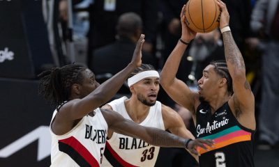 Dylan Harper (d) de Spurs recibe la marca de Jrue Holiday (i) y Toumani Camara de Trail Blazers durante el juego de este domingo en el AT&T Center de San Antonio (Texas. EFE/ Carlos Ramírez