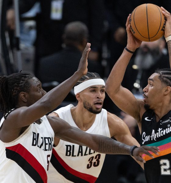 Dylan Harper (d) de Spurs recibe la marca de Jrue Holiday (i) y Toumani Camara de Trail Blazers durante el juego de este domingo en el AT&T Center de San Antonio (Texas. EFE/ Carlos Ramírez