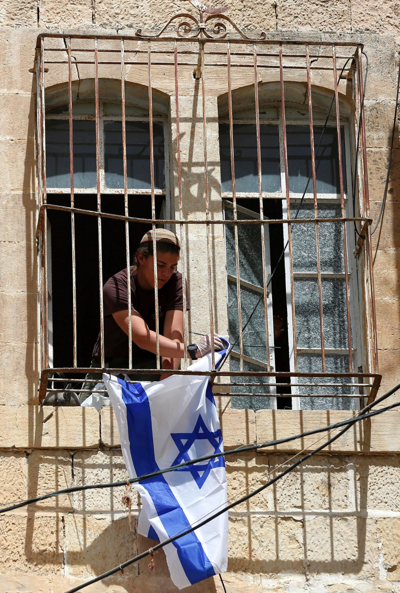 Imagen de archivo de un colono judío que cuelga una bandera israelí en una de las ventanas de un edificio palestino cerca de la mezquita de Ibrahimi, en la ciudad cisjordana de Hebrón. EFE/ Abed Al Hashlamoun