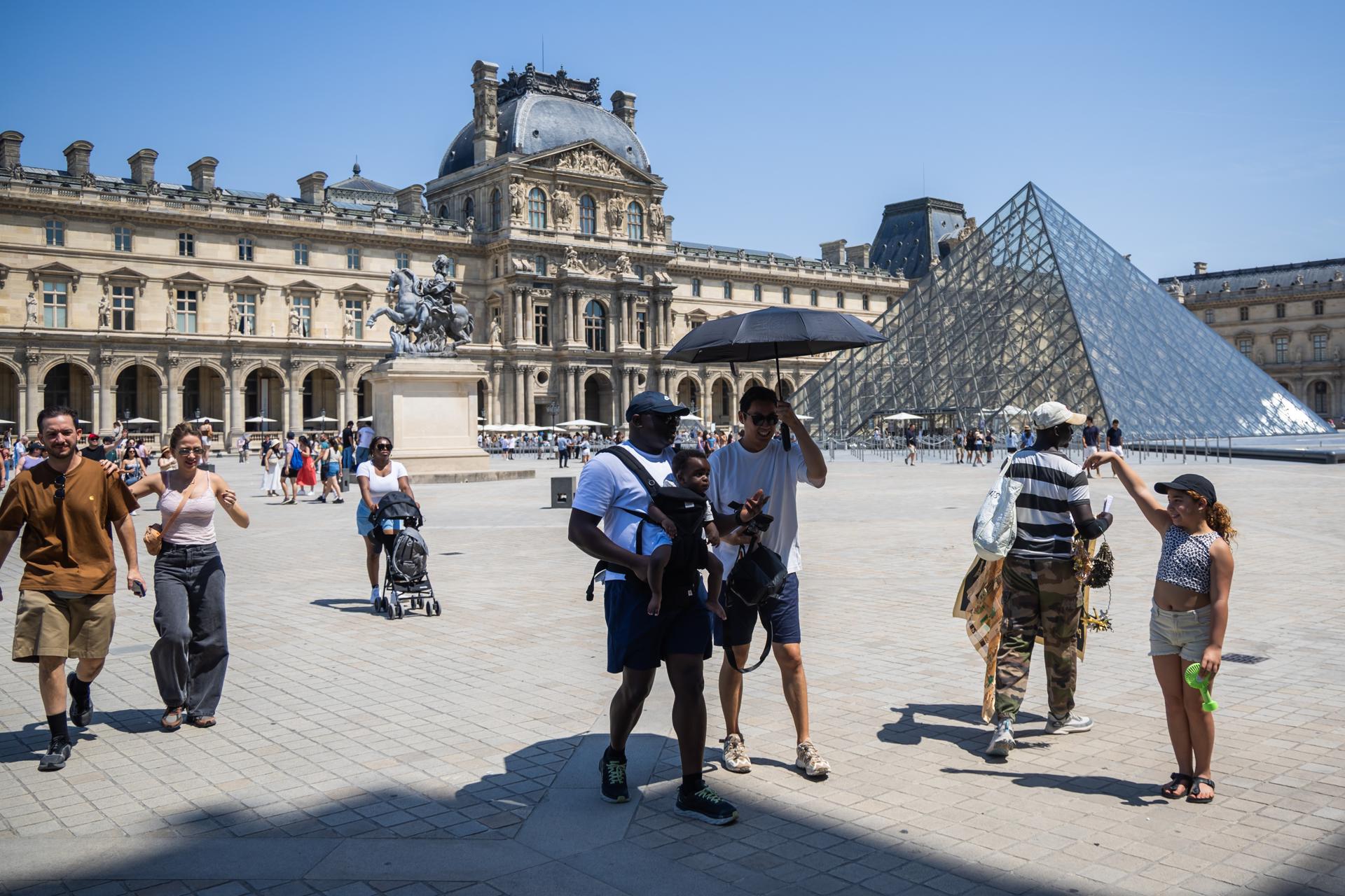 Personas se protegen del sol con paraguas frente al Museo del Louvre en París, este sábado. EFE/EPA/CHRISTOPHE PETIT TESSON