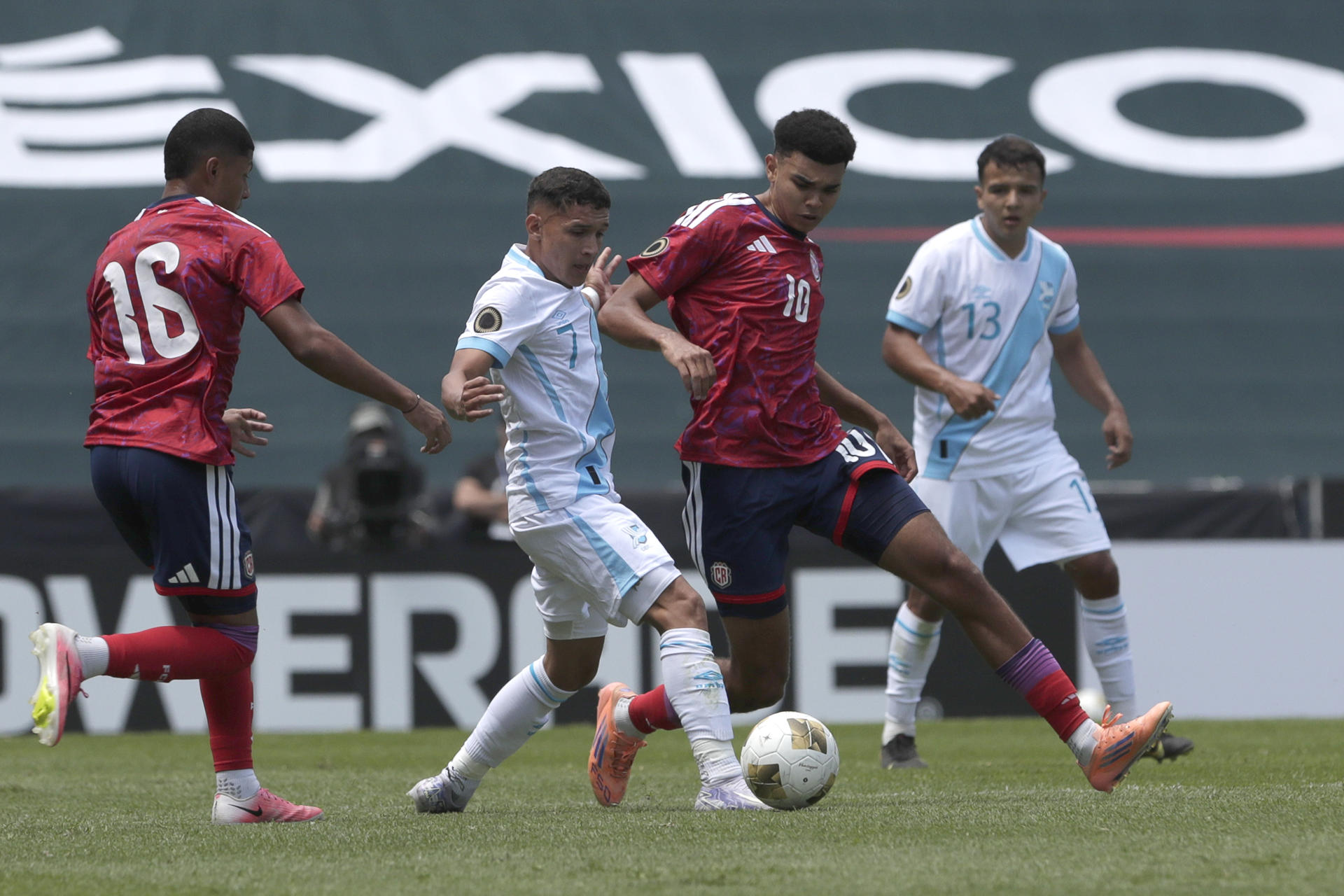 El guatemalteco Yordi Aguilar (c) disputa el balón con el costarricense Dax Palmer (2-d) durante el partido de la primera jornada del torneo sub-20 de la Concacaf, clasificatorio para los Juegos Olímpicos de Los Ángeles 2028 que se jugó este viernes en el estadio Cuauhtémoc en Puebla. EFE/ Hilda Ríos