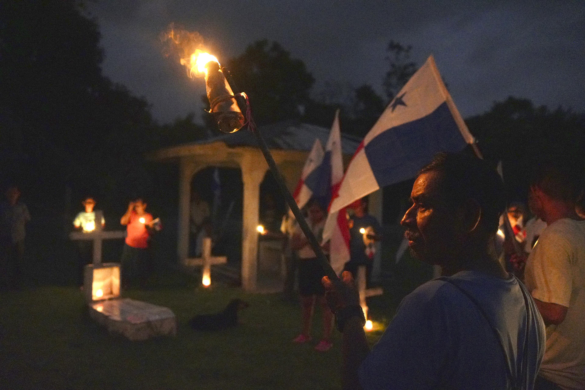 Campesinos sostienen banderas y velas en una vigilia en rechazo al decreto ejecutivo que ordena la clausura de los cementerios comunitarios para dar paso a la construcción del embalse de Río Indio, proyecto impulsado por el Canal de Panamá en la comunidad de Limón de Chagres (Panamá). EFE/Aris Mariota