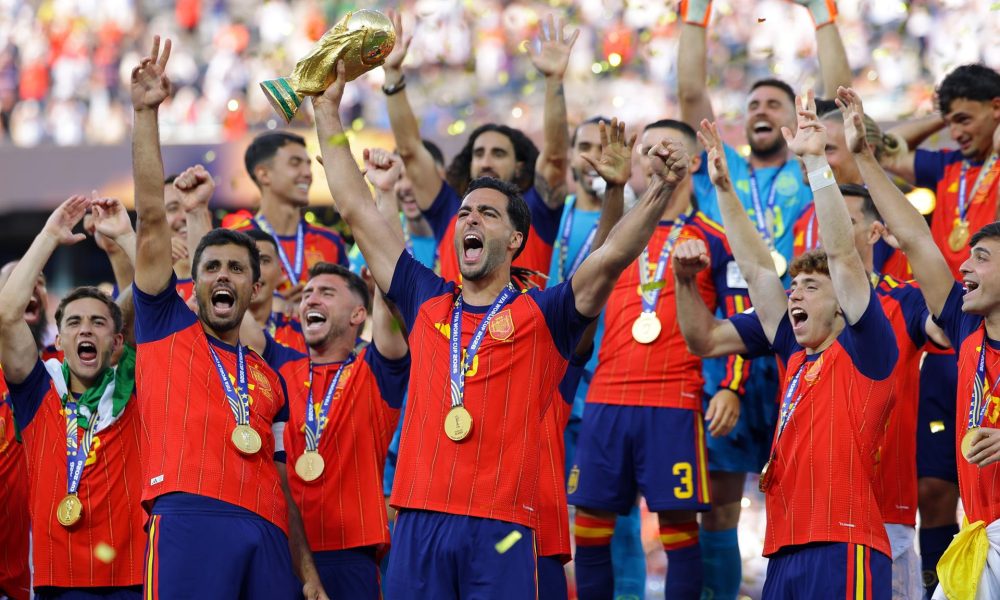 El español Mikel Merino levanta el trofeo de la Copa del Mundo mientras el equipo celebra tras ganar la final de la Copa Mundial de la FIFA 2026. EFE/EPA/CHRISTOPHER NEUNDORF