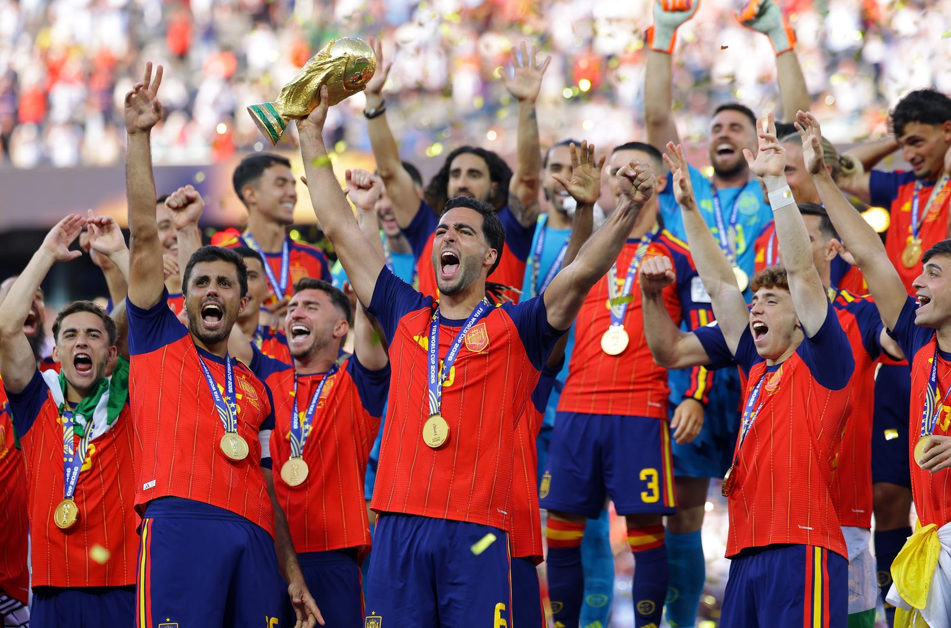 El español Mikel Merino levanta el trofeo de la Copa del Mundo mientras el equipo celebra tras ganar la final de la Copa Mundial de la FIFA 2026. EFE/EPA/CHRISTOPHER NEUNDORF