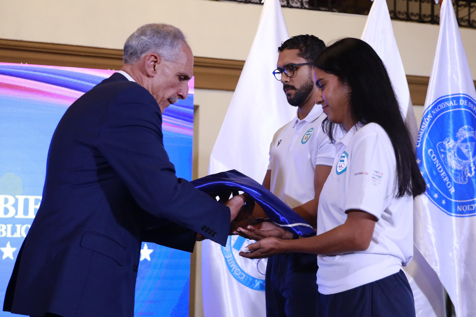 Fotografía cedida por Casa Presidencial de Honduras que muestra al presidente de Honduras, Nasry Asfura (i), entregando una bandera a deportistas que integran la delegación que representará al país en los XXV Juegos Centroamericanos y del Caribe este miércoles, en Tegucigalpa (Honduras). EFE/ Casa Presidencial de Honduras