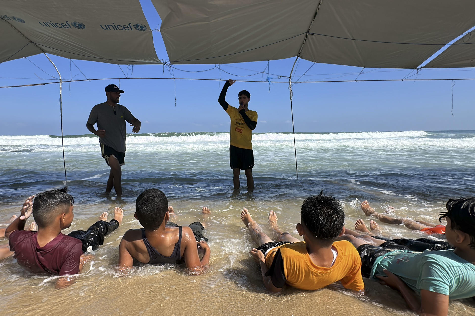 Bajo toldos improvisados con lonas de Unicef, más de una treintena de niños se zambullen en el mar en Gaza y aprenden a flotar acompañados de un grupo de monitores. EFE/Str
